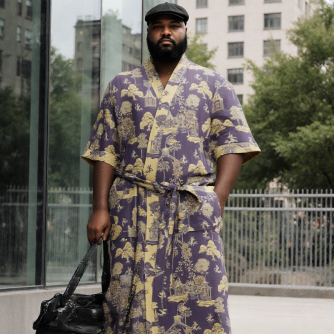 Man wearing a purple and yellow patterned robe with a black cap, standing outdoors. (Blue)