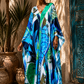 A woman wearing a vibrant, multicolored abstract print kaftan dress with blue, green, and white patterns, standing in front of a rustic beige wall and a teal wooden door.