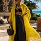 Woman in black outfit with yellow cover-up standing on a sunlit patio.(Yellow)