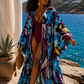 flowy floral kimono cover-up over a deep burgundy one-piece swimsuit. The cover-up has a bold tropical floral pattern in blue, purple, yellow, and white.