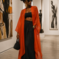 Woman in an orange cardigan and black dress standing in an art gallery. (Orange)