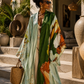 Woman in a colorful dress standing in an outdoor setting with plants and architectural elements. (Green)
