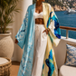 Woman in a colorful kimono standing on a balcony with a scenic view of water and mountains. (Blue)