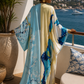 Woman in a colorful dress standing on a balcony with a scenic view of the sea and mountains. (Blue)