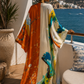 Woman in a colorful dress standing on a balcony with ocean view (Orange)
