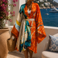 Woman in colorful kimono standing by a scenic coastal area with flowers and a boat. (Orange)