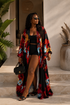 Woman wearing a colorful floral kimono over a black outfit, standing on steps with plants and a pot in the background.