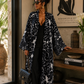 Woman in a black and white patterned coat standing in a room with decor elements.