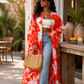 Woman wearing a red and white floral kimono with blue jeans, standing outdoors.
