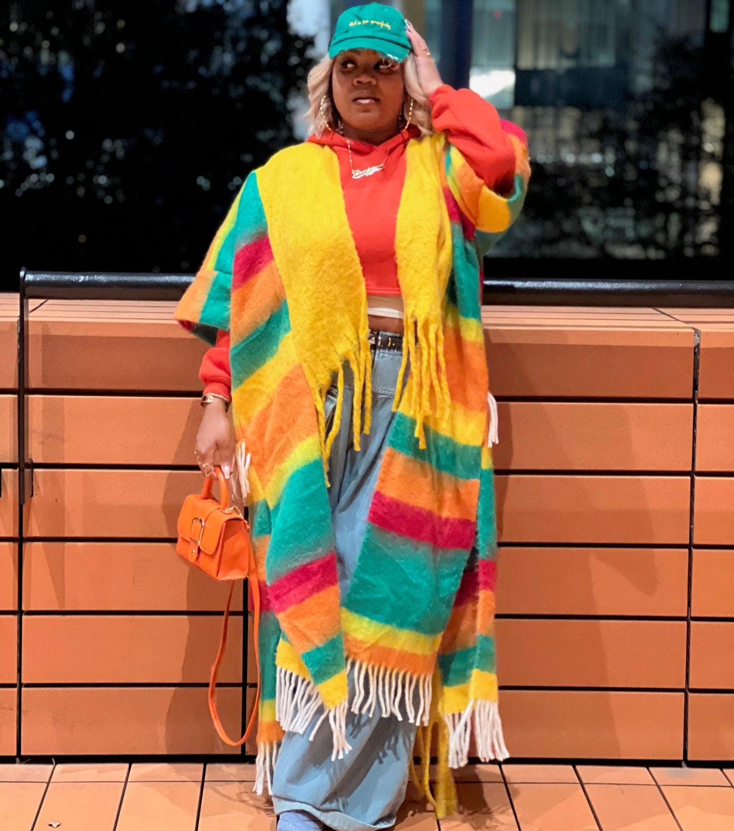 Person wearing a colorful striped shawl and red jacket in an urban setting. (Yellow)