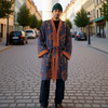 Man wearing a patterned robe and green beanie standing on a city street. (Blue)