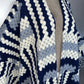 A close-up of a textured knit cardigan featuring a geometric pattern in navy blue, cream, and light blue-gray, displayed on a neutral mannequin torso. (Grey)