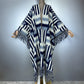 A knitted open-front poncho with wide draped sleeves and long fringe, displayed on a mannequin against a plain light gray background. The garment has a geometric zigzag pattern in navy, white, and light gray, (Grey)