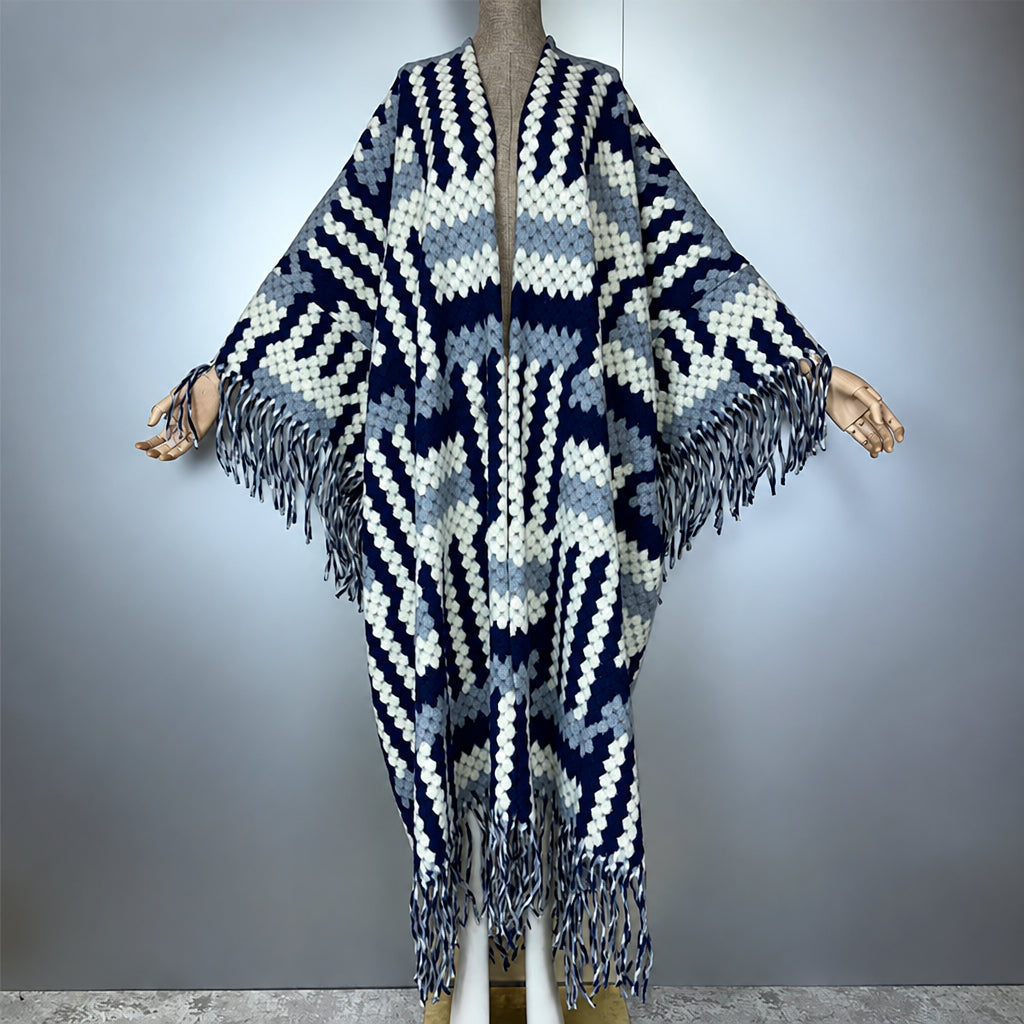 A knitted open-front poncho with wide draped sleeves and long fringe, displayed on a mannequin against a plain light gray background. The garment has a geometric zigzag pattern in navy, white, and light gray, (Grey)