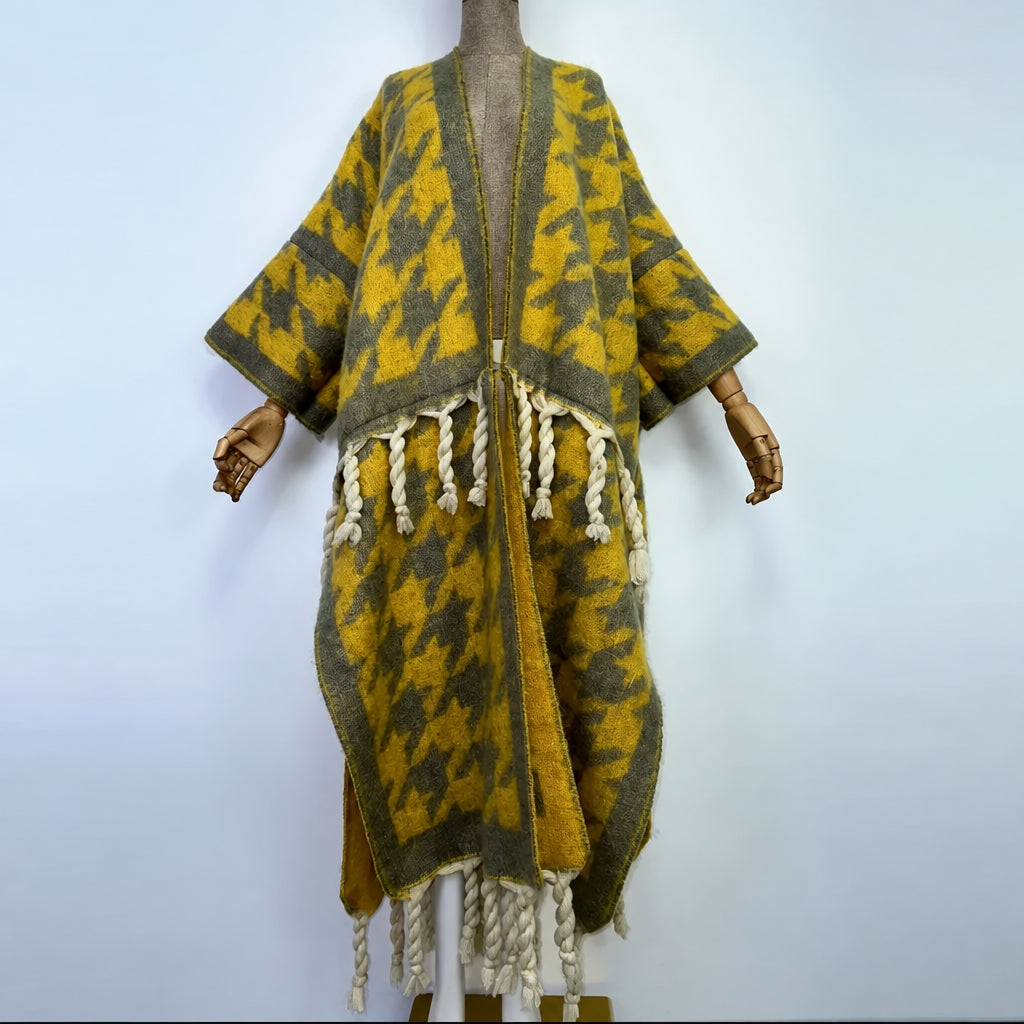 A yellow and gray patterned open-front poncho or cardigan with cream braided fringe, displayed on a mannequin against a plain light background. (Yellow)