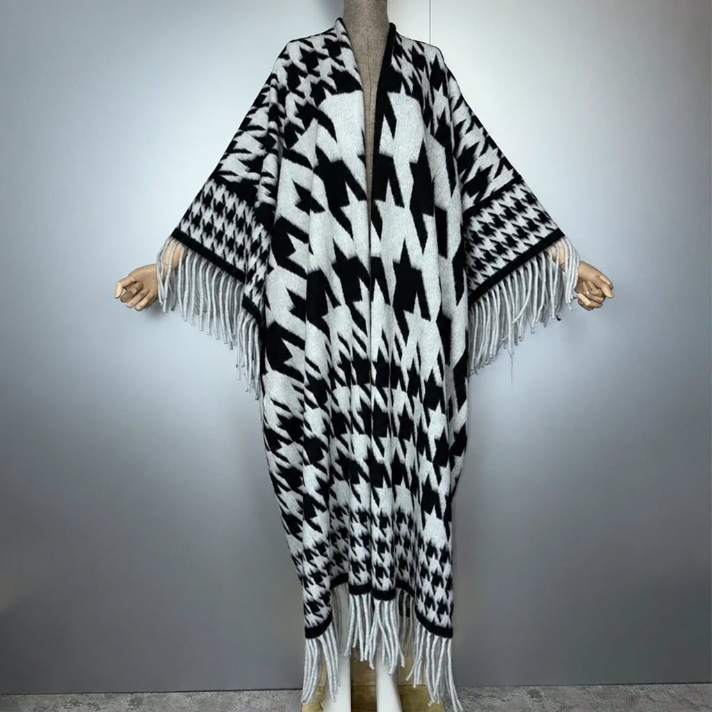 A black and white patterned knit poncho with fringe trim displayed on a mannequin against a gray studio background. The brand name 'winyi' is visible in the top left corner.